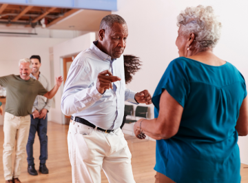 Seniors enjoying a lively dance class in a bright studio with a wooden floor.