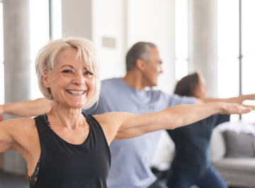 Senior woman smiling during group yoga session, practicing warrior pose. Fitness and wellness lifestyle.